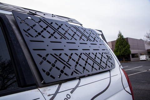 2004 Subaru Forester window with a black molle panel in a parking lot.