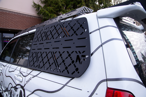 Black molle panel car roof rack on a white subaru forester with trees and a building in the background