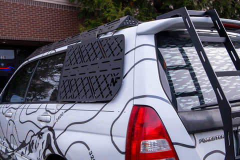 White Subaru Forester with black roof rack and rear window molle panel, parked outdoors.