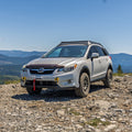 A white Subaru off-road Crosstrek parked on a rocky mountain trail with a scenic valley and blue sky in the background.